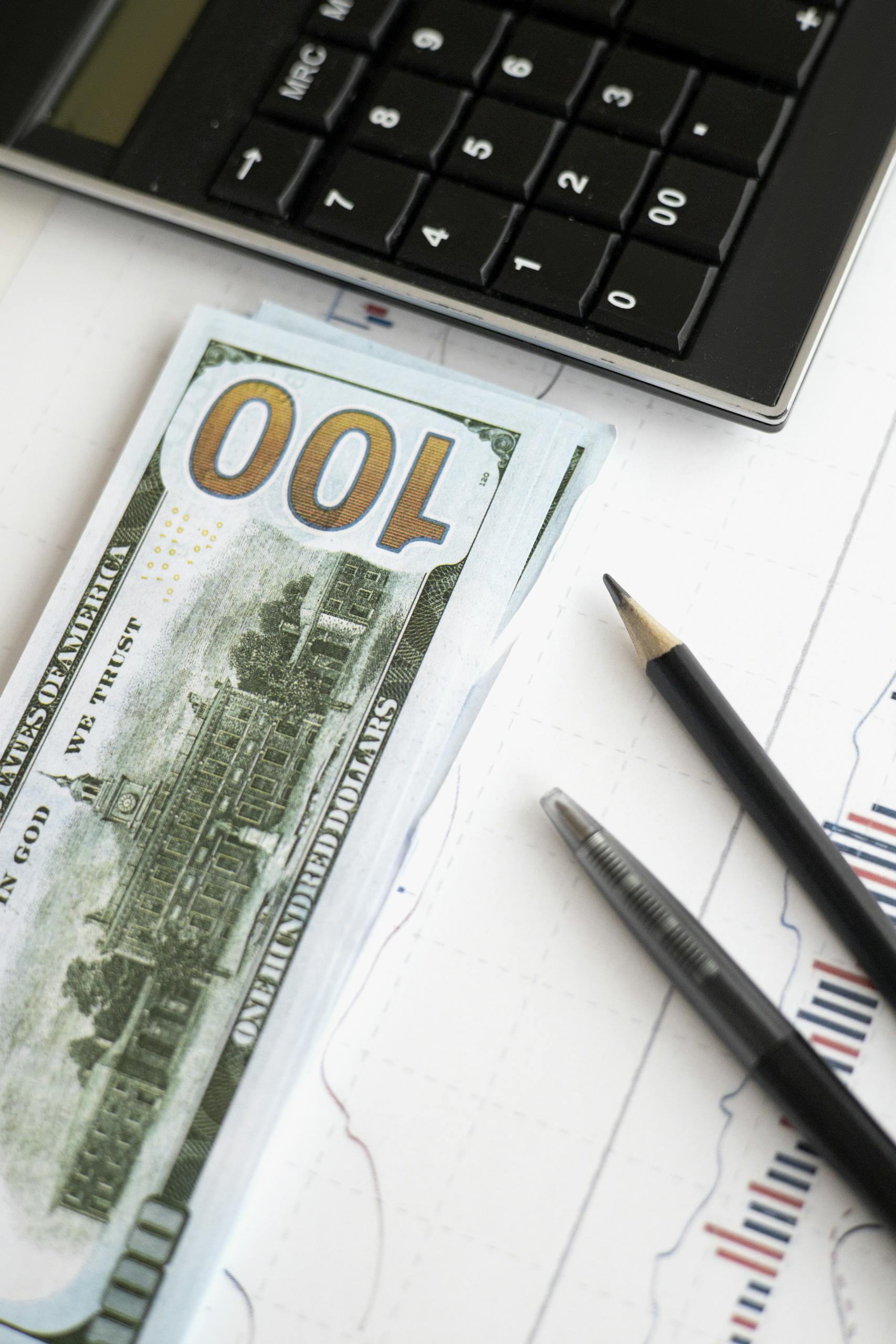 Stack of hundred dollar bills beside calculator and graph for financial analysis